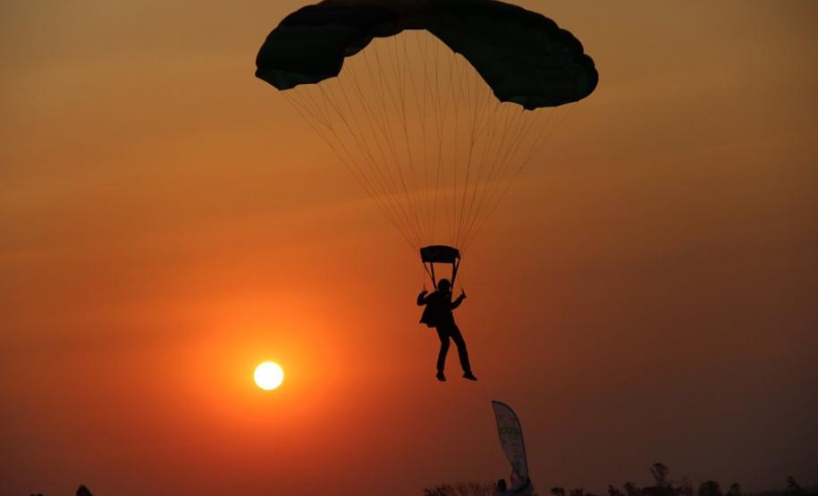 Pouso de um paraquedista no fim da tarde, com pôr-do-sol.