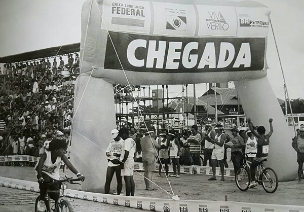 Em uma das atividades de ciclismo, público na arquibancada assiste os participantes alcançando a linha de chegada. 