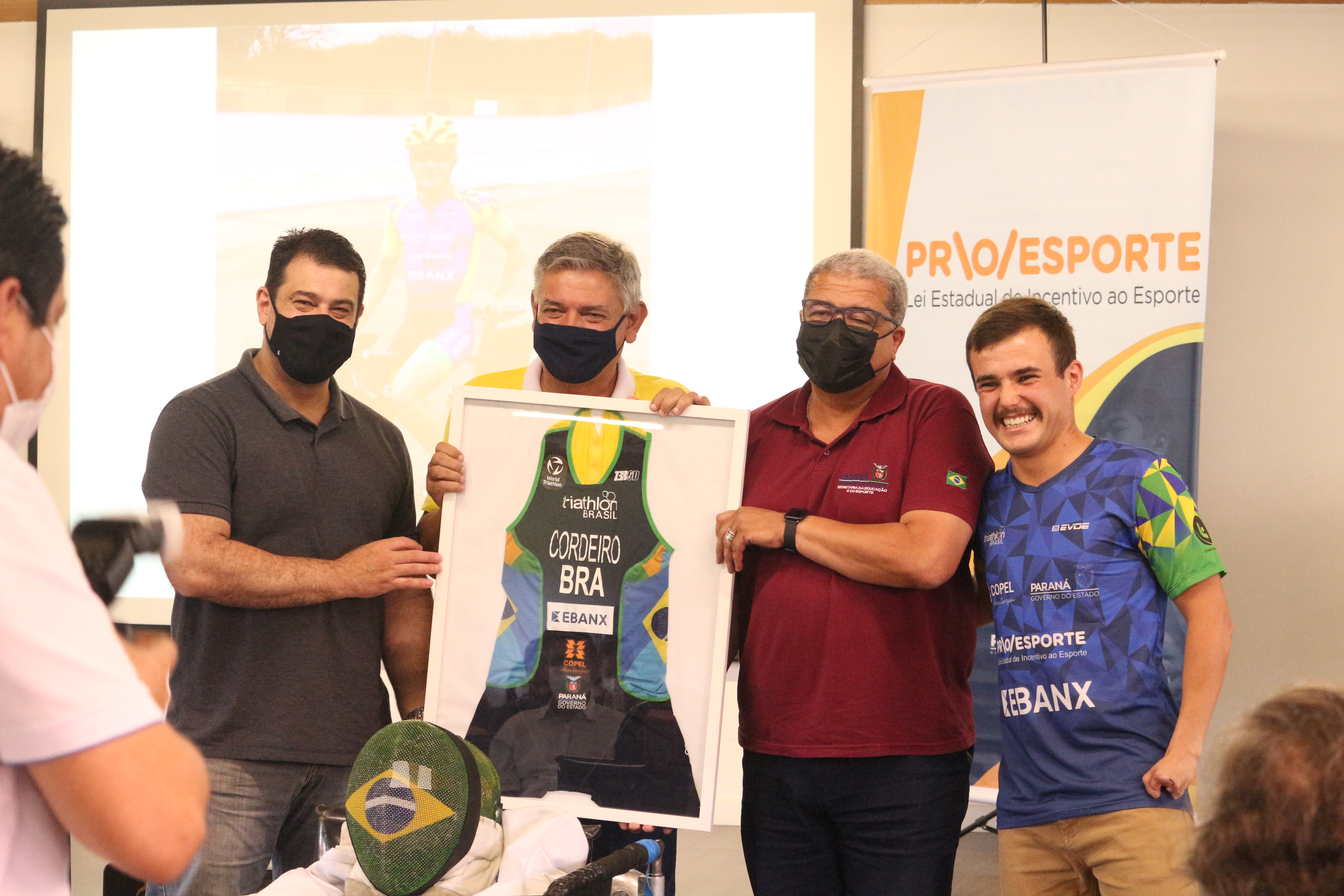 Na foto, da esquerda para a direita, o Deputado Alexandre Amaro, o Superintendente Geral do Esporte, Helio Wirbiski, Jose Alberto de Campos e o o atleta, Ronan Cordeiro, que presenteou Wirbiski com seu uniforme de competição. 