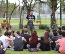 Professor em pé repassando orientações para acadêmicos que estão sentados na grama.